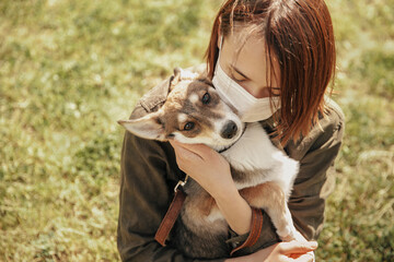 Woman in protective mask hugs her dog on the street