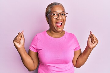 Senior african american woman wearing casual clothes and glasses screaming proud, celebrating victory and success very excited with raised arms - Powered by Adobe