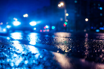 Rainy night in the big city, the approaching car headlights shine through the mist. Close up view from the level of the dividing line