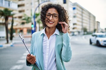 Young hispanic business woman wearing professional look smiling confident at the city holding...