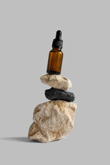 Brown dropper glass pipette bottle balancing on rocks, gray background, copy space. Serum, oil,...