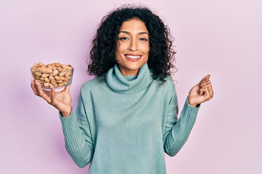 Young latin girl holding peanuts screaming proud, celebrating victory and success very excited with raised arm