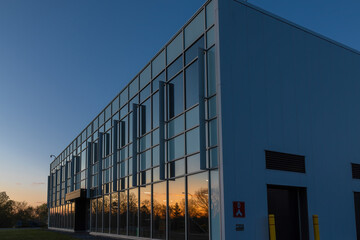 Low-rise commercial or institutional building glass and aluminum facade at dusk with sunset reflecting on windows, security cameras, nobody