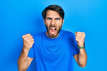 Fototapeta premium Young hispanic man wearing casual clothes angry and mad raising fists frustrated and furious while shouting with anger. rage and aggressive concept.