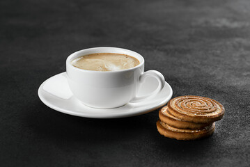 White cup with cappuccino coffee and cookies on a black background.