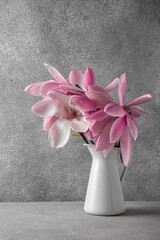 Pink magnolia flowers bouquet in vase on gray concrete background. wedding or holiday concept. vertical orientation