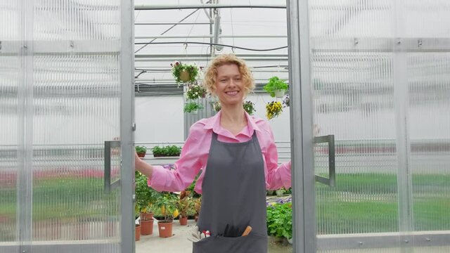 Happy blonde florist gardener enjoys working in her greenhouse walking through flower saplings