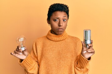 Young african american girl holding lightbulb for inspiration and idea skeptic and nervous,...
