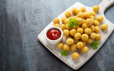 Crispy potato balls with ketchup on white wooden board