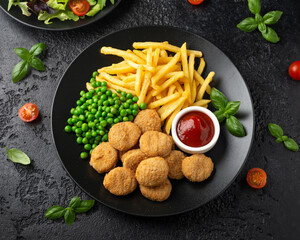 Fried crispy chicken nuggets with ketchup, french fries and green peas in black plate
