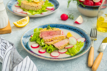 Tuna steak in a sesame crust with fresh salad on a blue ceramic plate on a light background concrete. Fish, seafood recipes