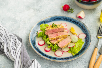 Tuna steak in a sesame crust with fresh salad on a blue ceramic plate on a light background concrete. Fish, seafood recipes