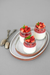 Italian dessert panna cotta with fruit jelly and fresh pieces of strawberries on gray background. Copy space