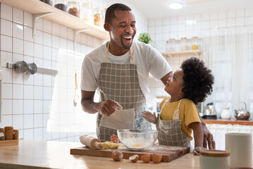 Happy Black African American Father and little son smiling and laughing while cooking in kitchen.
