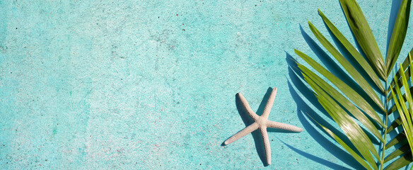 Fototapeta na wymiar Starfish with tropical palm leaves on blue cement background. Summer background concept.
