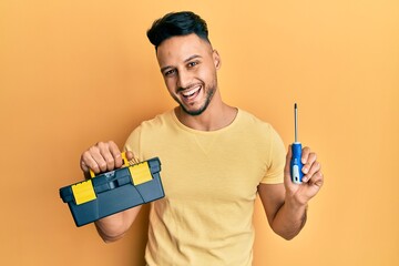 Young arab man holding toolbox and screwdriver smiling and laughing hard out loud because funny crazy joke. - obrazy, fototapety, plakaty