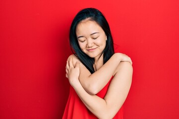 Young chinese girl wearing casual clothes hugging oneself happy and positive, smiling confident....