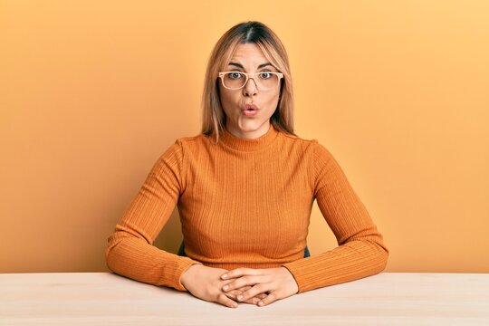 Young caucasian woman wearing casual clothes and glasses sitting on the table scared and amazed with open mouth for surprise, disbelief face