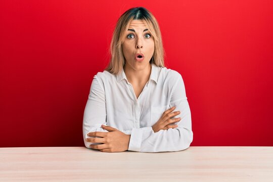 Young caucasian woman wearing casual clothes sitting on the table afraid and shocked with surprise expression, fear and excited face.