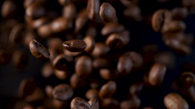 Roasted coffee beans in slow motion. Coffee beans in a free fall. Floating in the air on dark background. 