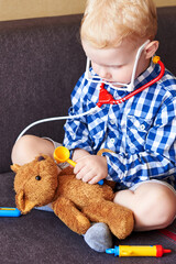 Little boy playing doctor with toy tools and teddy bear.