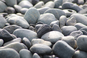 Round stones on a dry river bed outside in nature. Smooth pebbles with light gray tones in ambient light.
