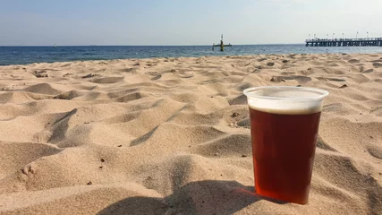 Papier Peint photo La Baltique, Sopot, Pologne A beer in a plastic cup located on the sandy beach in Gdynia, Poland. In the back there is a small pier going into the calm Baltic Sea. relaxing and chilling at the beach. Beer to go.