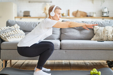 Senior woman stretching, online training in living room. Balancing yoga exercise. Exercising for...
