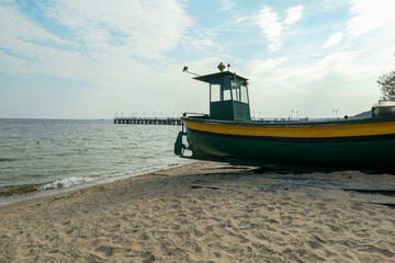 A colorful boat parked on the sandy beach in Gdynia, Poland. In the back there is a small pier...