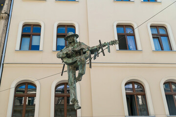 A figure of a man playing the guitar handed above the street in Katowice, Poland. In the back there is a tall building. The monument is handed on a metal rope. Modern art. - obrazy, fototapety, plakaty