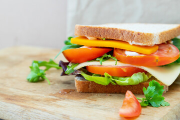 Tasty sandwich with cheese, arugula, tomatoes, lettuce and parsley on a wooden cutting board. View from the side, copy space.