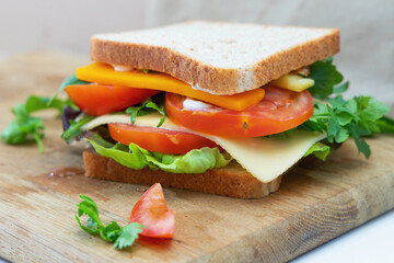 Tasty fresh sandwich with cheese, arugula, cheese, tomatoes, lettuce and parsley on a wooden cutting board.