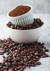 Two bowls on top of each other with fresh raw coffee beans and powder on light background.