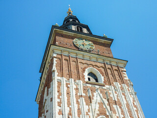 A close up on the tower of St. Mary's Basilica in Cracow, Poland. The tower is contrasted with blue sky. There is a clock at the top of the tower. A few windows.