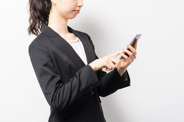 白バックの前に立って、スマホを使うビジネスウーマン