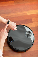 Faceless middle section of young woman touching an smart watch to control an automatic vacuum cleaner to clean the floor, controlling smart machine housework robot with smart phone app