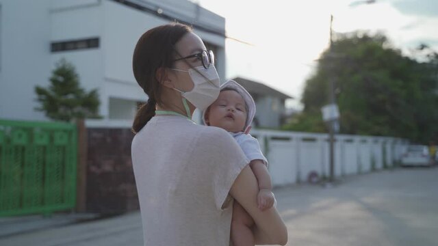 Young Happy Asian Woman Mother Walking Outdoor Holding Baby Infant Around Neighbor. Woman In Medical Face Mask Walk Village Street In Evening During Covid 19. Natural Authentic.