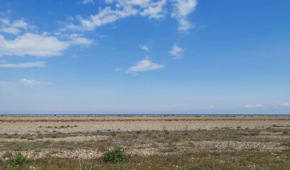 Fototapeta na wymiar Deserted marshland beach with rough ground in foreground and sea on horizon