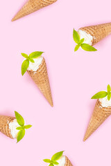 Mint vanilla ice cream with in a waffle cone with mint leaves on a pink plain background.