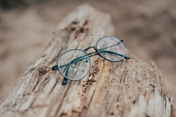 Womens beautiful glasses lie on a narrow beam on the beach on a blurred background