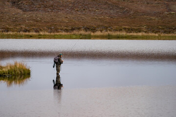 Fototapeta na wymiar Fisherman alone stand in river water. Hobby sport activity. Fisherman fishing equipment. Reflection in Loch Long.