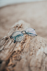 Fototapeta na wymiar Womens beautiful glasses lie on a narrow beam on the beach on a blurred background