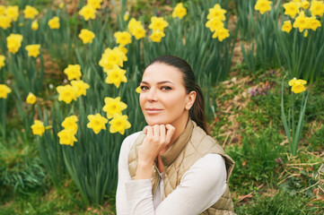 Spring portrait of young beautiful woman sitting in a field of blooming daffodils