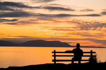 Obraz premium Silhouette of a man sitting on a bench at beautiful sunset. View of the Isle of Skye. Scotland landscape. 