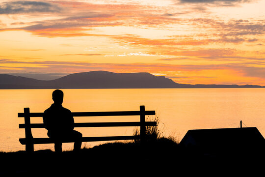 Silhouette of a man sitting on a bench at beautiful sunset.  View of the Isle of Skye. Scotland landscape. 