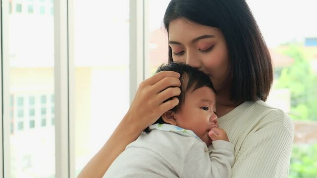 Happy young asian mom holding cute adorable infant child in livingroom. Cheerful adult mother lull a kid baby having love together in home. Parents and daughter activity,