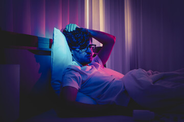 Depressed insomnia white man holding his head on a bed late at night with Black Medical pills for...