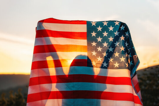 Independence day. Silhouette of woman holds an American flag in her hands, raised above her head. Back view. In the background, sunset and mountains. The concept of American National Holidays