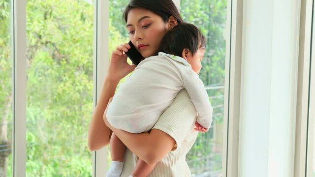 An Asian family mother holds her baby while talking on the phone for business. Work in parallel with raising babies for the family.