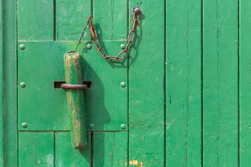 Holzpflock an Kette zum Verschließen einer grünen Stalltür